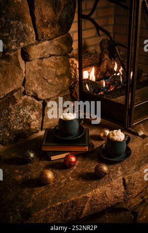 Fireplace with books, mugs with whipped cream on Christmas decorations on hearth Stock Photo