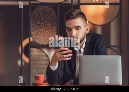 Portrait of young happy business man sitting at his desk in the modern office and using a phone. Stock Photo