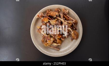 A top-down view of a plate filled with leftover chicken bones on a dark table. The image highlights the remnants of a meal in a casual dining setting. Stock Photo