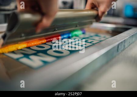 Close up of graphic worker's hands using rubber blade and pressing ink while silkscreen printing at printing workshop. Cropped picture of graphic work Stock Photo