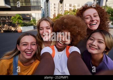 Happy multiethnic young women friends using phone to take a selfie with a smartphone together. Stock Photo