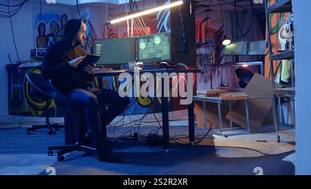 Man arriving in underground bunker, using it to mask his location while committing international espionage. Spy using tablet and computer systems to steal governmental secrets Stock Photo