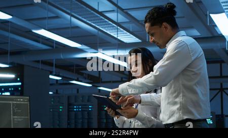 Team of technicians working on tablets in data center used for managing gear energy consumption. Teamworking colleagues using devices in workspace used for automation in server farm Stock Photo