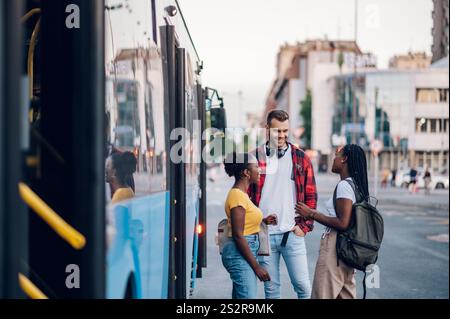 Diverse group of friends waiting for a bus while at a bus stop. Riding, sightseeing, traveling to work, city tour, togetherness. Multiracial group of Stock Photo