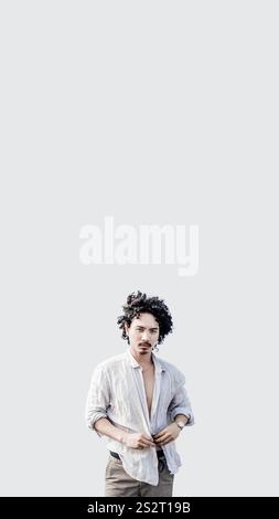 A vertical mobile-friendly format shot of a stylish biracial young man with curly hair on the white solid background, wearing an open linen shirt and Stock Photo