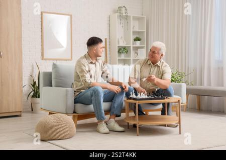 Young man with his father playing chess on sofa at home Stock Photo