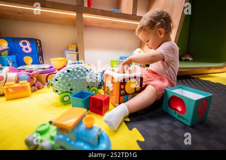 Toddler engaged with building blocks and interactive toys in a cheerful play area Stock Photo