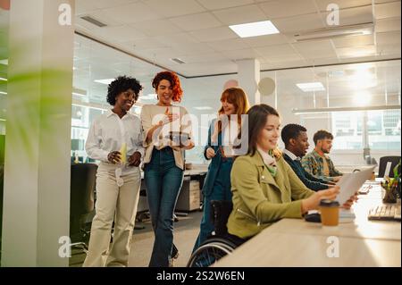 Diverse coworkers are bringing a birthday cake to a woman who uses a wheelchair and surprising her. Inclusive colleagues surprising a businesswoman in Stock Photo