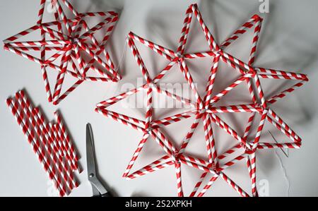 Set of handmade stars in red and white stripe. Different shape. Chaotically placed on white background. Needle, white thread, scissors, paper straws for drinks are nearby. Idea for decoration. Photo. Stock Photo