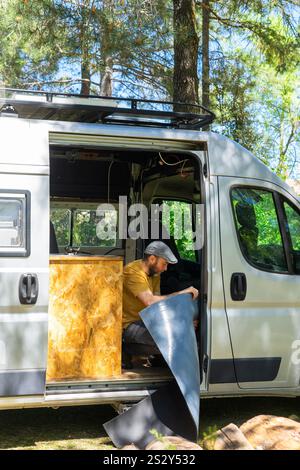 Concentrated man installing insulation material inside his campervan during a conversion process in a forest Stock Photo