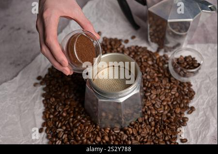 Woman's hands pouring coffee from a small transparent cup in geyser coffee maker moka machine. Scattered fresh aromatic coffee beans around Stock Photo