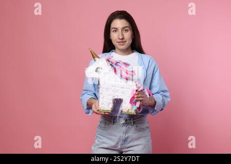 Woman with unicorn shaped pinata on pink background Stock Photo