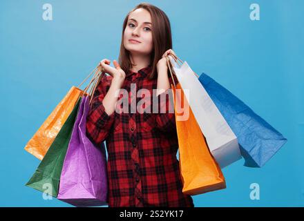 A happy young woman poses confidently with multiple colorful shopping bags. Stock Photo