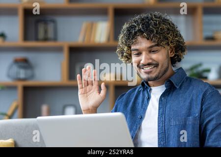 Man at home on sofa using laptop for video call, young student waving happily at online conference meeting. Stock Photo