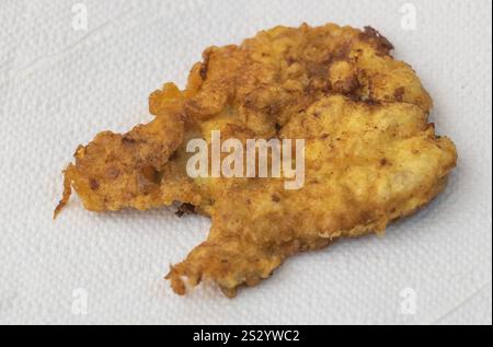 Close-up of an extremely small piece of fried chicken on white paper. Stock Photo