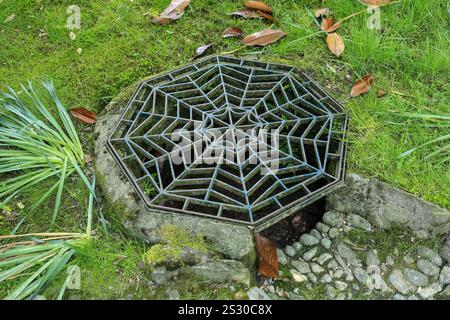 A drainage grid cover in the shape of a spiders web. Stock Photo