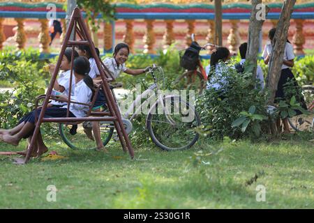 Kandal Province, Cambodia. Jan 08,2025: Schoolgirl on a bike & her friends on a swing in schoolyard. Back to school for Khmer children in Phnom Penh suburbs, later than in other Southeast Asian countries. Yesterday was a public holiday, as Cambodians celebrated Victory over Genocide Day on January 7, 1979, with the liberation of the capital & the fall of the Pol Pot regime. Although the country is predominantly Buddhist (93% to 97%), the 'winter' school vacations include Christmas, Cambodian Peace Day on December 29, International New Year and Victory Day. Credit: Kevin Izorce/Alamy Live News Stock Photo