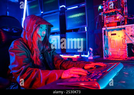 Woman hacker. Asian woman wearing hood is typing keyboard for coding hacking programming system Stock Photo