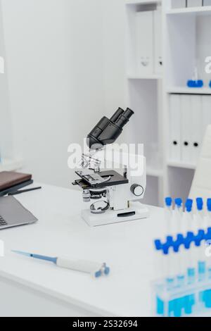 A modern laboratory setup featuring a high-powered microscope positioned on a clean white table. Surrounding the microscope are test tubes filled with Stock Photo