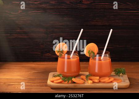 On the cutting board are two glasses with freshly squeezed juice and straws. Carrots and leaves that have been sliced. The sun's rays illuminate the w Stock Photo