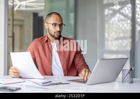 Serious focused businessman doing paperwork inside office, man in casual shirt working with documents contracts and reports, successful financier investor. Stock Photo