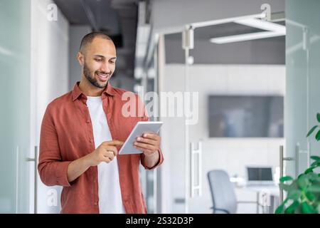 Successful satisfied businessman using tablet computer inside office at workplace, man in casual shirt reading online report, programmer developer testing new software. Stock Photo
