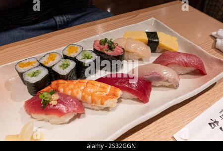 A pristine white plate beautifully adorned with a delightful variety of sushi selections is sitting elegantly on the table Stock Photo