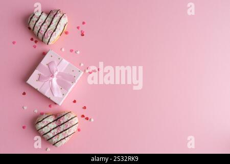 Two heart-shaped Donuts and gift box on pink background with hearts topin decoration. Copy space. Top view. Stock Photo