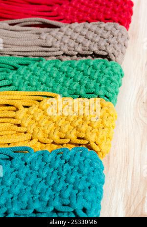 Small bags knitted using the macrame technique from cotton cord. Multi-colored bags for mobile phones on a wooden background. Stock Photo
