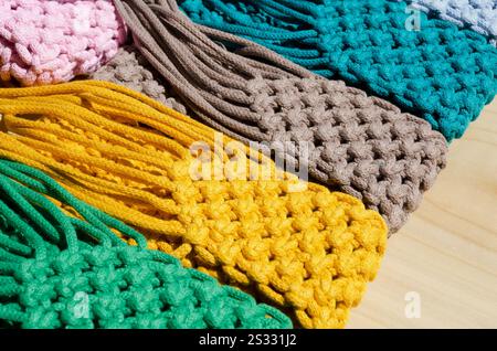 Small bags knitted using the macrame technique from cotton cord. Multi-colored bags for mobile phones on a wooden background. Stock Photo