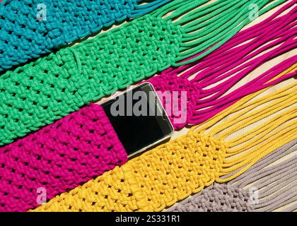 Small bags knitted using the macrame technique from cotton cord. Multi-colored bags for mobile phones on a wooden background. Stock Photo
