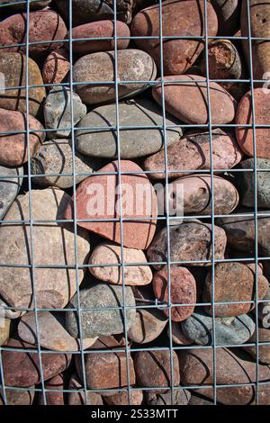 Colorful river rocks arranged behind a metal wire grid, showcasing natural textures and earthy tones for a rustic, decorative look. Stock Photo