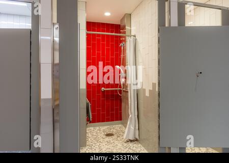 New single, private, gym locker room shower with red tile wall, bench, tile floor, and white shower curtain. Stock Photo