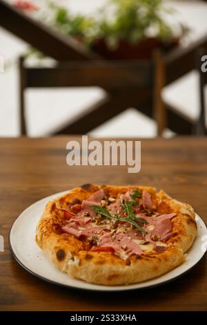 Delicious full ham pizza served on outdoor restaurant table, close-up food photography of Italian cuisine meal on a plate outdoors, outside, no people Stock Photo