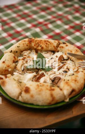 a delicious chicken and mushrooms pizza on tablecloth , sliced served on a wooden board with a backdrop of a burlap tablecloth scattered with cherry t Stock Photo