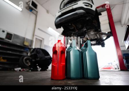 Car oil containers in a mechanic's shop with a vehicle lifted on a hydraulic jack. Represents auto maintenance, repair, and service environment. Stock Photo