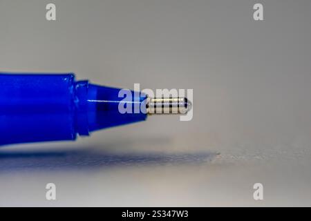 A blue pen with a silver tip is shown in the image. The pen is placed on a white surface, and the tip is pointing upwards. The pen appears to be a bal Stock Photo