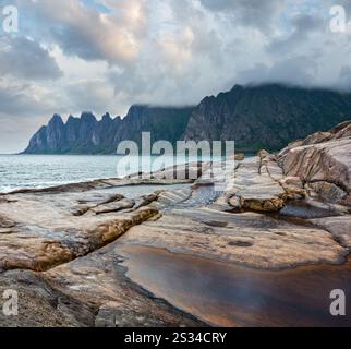 Stony beach with tidal baths at Ersfjord, Senja, Norway. Summer polar day night coast. The dragon teeth rock in far. Stock Photo