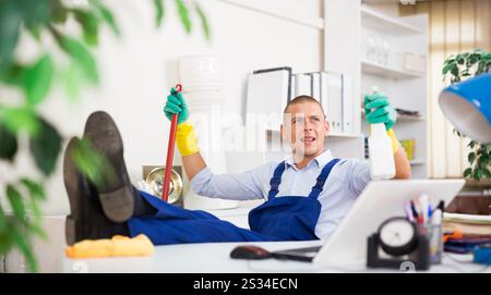 Relaxed cleaning service worker sitting in office with feet on table Stock Photo