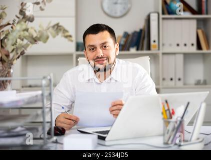 Positive man bookkeeper doing paperwork in office Stock Photo