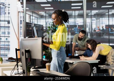 Company personnel sitting at desks in office, imputing data on computers. Woman typing on laptop keyboard next to staff members in modern relaxed workplace solving tasks during job shift Stock Photo