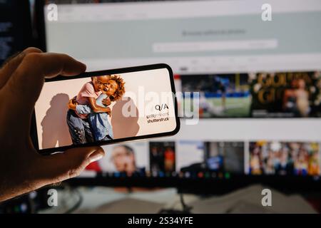 Paris, France - Jan 7, 2025: A smartphone displaying an image labeled Q and A Getty Images Shutterstock is held in front of a computer screen showing Stock Photo