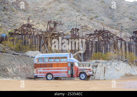 An old bus is parked in a desert. The bus is rusty and has a wooden frame. The desert is barren and desolate Stock Photo