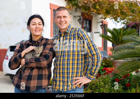 Smiling couple standing with cats near home Stock Photo