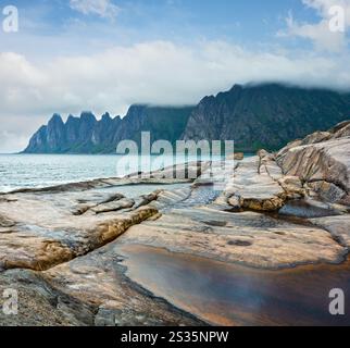 Stony beach with tidal baths at Ersfjord, Senja, Norway. Summer polar day night coast. The dragon teeth rock in far. Stock Photo