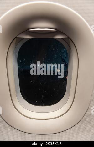 View from an airplane window as the plane sits on the tarmac during a thunderstorm. Rain water leaves a streak on the outside of the airplane window. Stock Photo