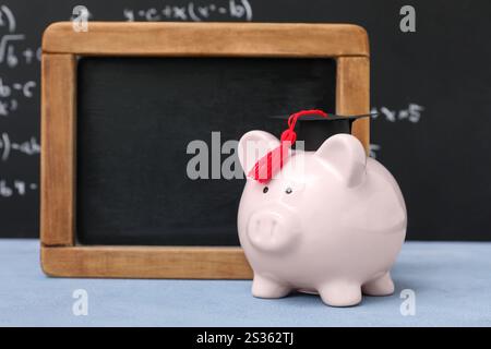 Piggy bank with graduation hat and blank chalkboard on table near blackboard. Student loan concept Stock Photo