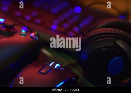 Modern gamepad and gaming mouse lies with keyboard and headphones on table in dark playroom scene close up. Video game challenges and competitions con Stock Photo