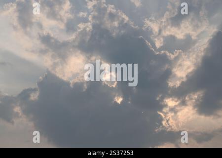 sunlight streaming across high clouds from behind lower dark clouds Stock Photo