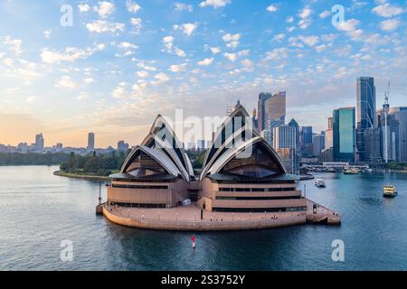 Sydney Opera House, designed by Danish architect Mr Jorn Oberg Utzon , at first light as the sun rises over Sydney harbour and city centre skyscrapers Stock Photo